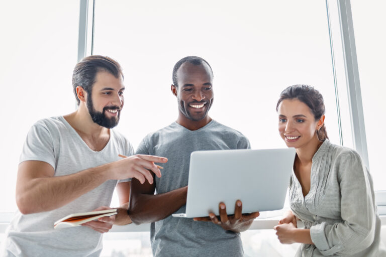 Three young co-workers using laptop and discussing new project at office, developing strategy for online business, explaining sharing ideas, preparing presentation, having brainstorming session. Rear view